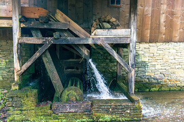 Side view of an old wooden building with a water wheel. A stream of water from a river forced on...