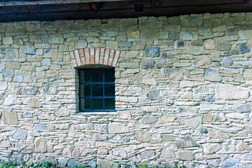 Detail of old building. Stone wall made of rough stones. Window with bars in blue color. Dirty window trim