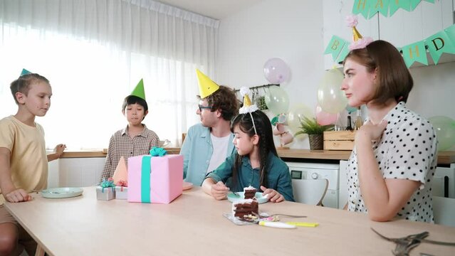 Attractive family celebrate daughter birthday while talking at modern kitchen decorated with colorful balloon while present placed on table. happy asian girl eating cake with smiling parent. Pedagogy.