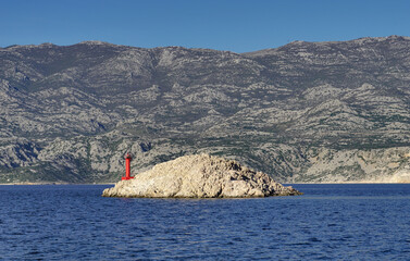 Stony island with small red lighthouse in front of massive mountains