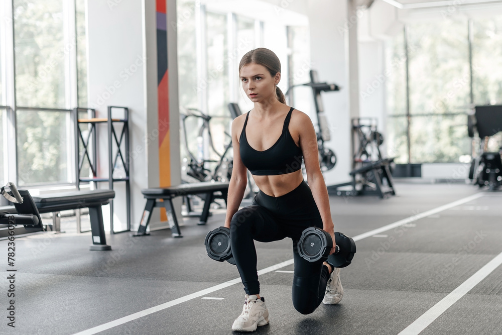 Wall mural fit woman does dumbbell squats in fitness gym