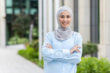 A portrait of a confident Muslim businesswoman wearing a hijab, smiling and standing outdoors with...