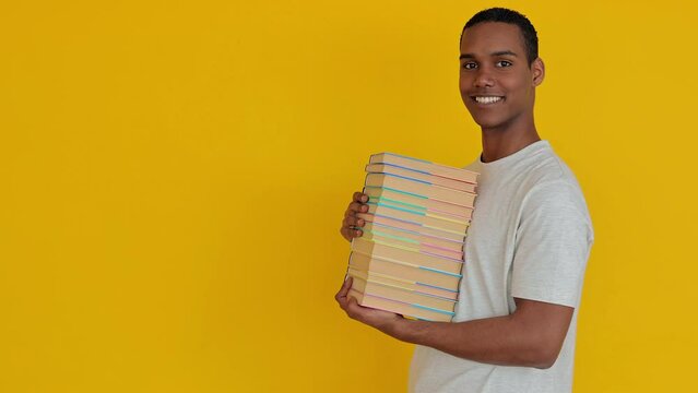 Smiling student boy holding academic books over yellow studio background. Education lifestyle concept.