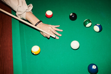 Top view closeup of male hand holding cue stick and playing billiard at green pool table with...