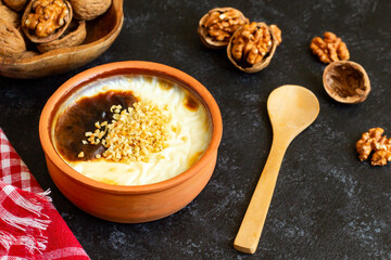 Baked rice pudding made with walnut milk, with walnuts in a casserole bowl, on a black surface.Vegan food