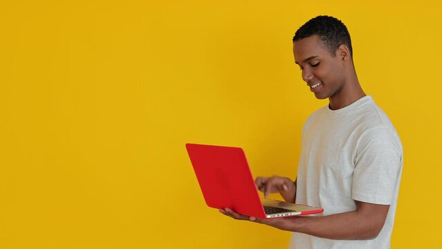 Happy african student man using laptop computer over yellow background. Education and technology concept. Copy space for text.