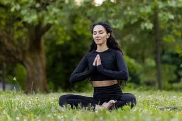 Fotobehang A serene Hispanic woman in a lotus pose meditates in a tranquil park setting, embodying peace and mindfulness. © Liubomir