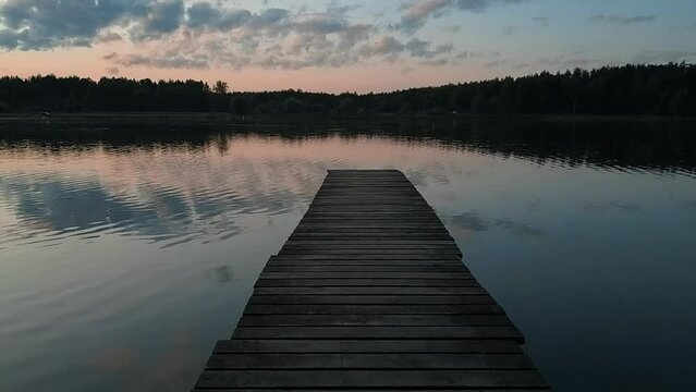 a slow motion to the end of a narrow wooden pier over a lake surrounded by dark wood HD  