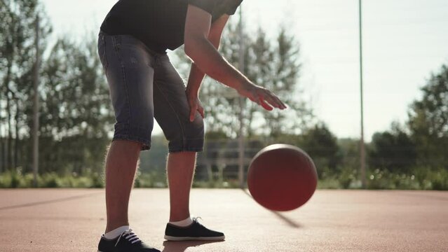Man dunks ball with hand on outdoor basketball court on sunny, picturesque day. Practice with sports equipment by amateur. Development of coordination and healthy lifestyle.