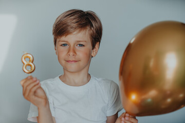 Portrait of handsome boy with birthday candle 8 and balloon