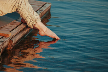 Woman foot touches surface of water at sunset light
