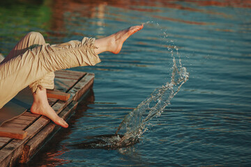Young woman sitting on a pier, splashing her feet in the lake water