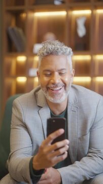 Joyful Businessman: Excited Man Celebrating Good News on Smartphone in Luxury Hotel. Happy Traveler Expressing Success and Happiness in Stylish lounge