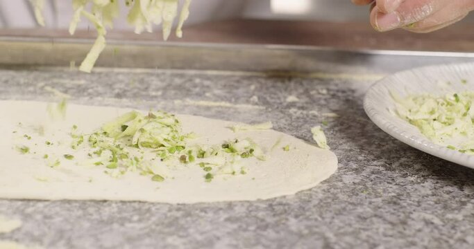 Traditional Turkish pide preparation. Chef puts the stuffing grated cheese and pistachios on the dough