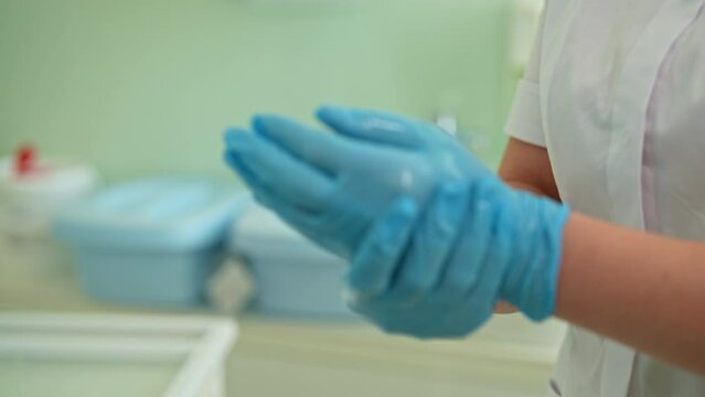 Close-up hands of unrecognizable woman nurse using antibacterial sanitizer on medical gloves at modern clinic. Concept of antiseptic disinfection, sterile work, infection protection, slow motion.