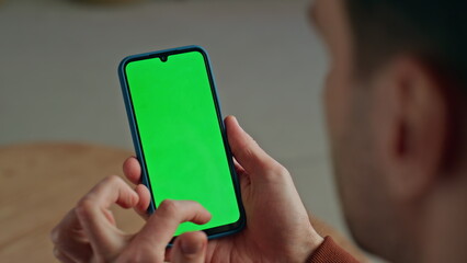 Unrecognizable man scrolling smartphone with green screen on workplace closeup