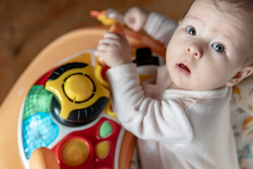 6 month old caucasian girl playing in a walker at home. Cute baby girl on a bouncer, family concept