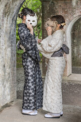 Two shy japanese women wearing kimonos.
Young ladies covering their faces with fox masks.
