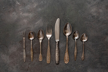 Old vintage cutlery in a row on a dark grunge background. Top view, flat lay.