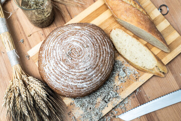 Freshly baked round bread and sliced baguette on a cutting board next to ears of wheat and a bread knife. High quality photo - obrazy, fototapety, plakaty