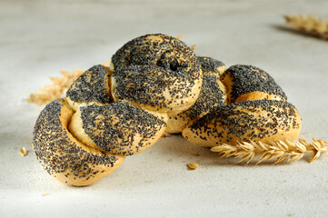 Braided buns sprinkled with poppy seeds close-up on a gray table. Selective focus, natural light