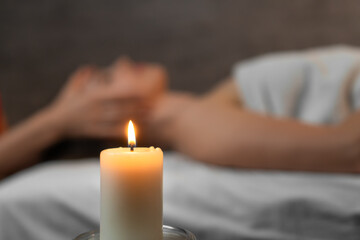 Close-up of a burning candle against the background of a blurred young woman on a massage at the spa sun. Concept of spa, health