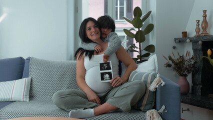 Mother and child posing for camera showing ultrasound of unborn baby during third trimester...
