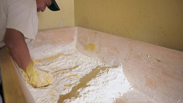Panadero latino integra los ingredientes para elaborar pan, en un recipiente de madera artesanal
