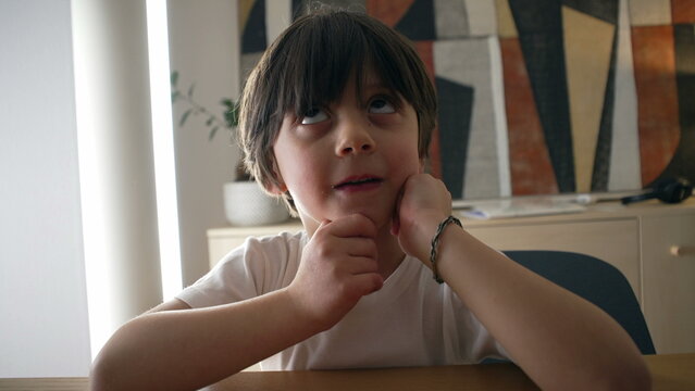 Pensive small boy pondering solution to a problem, close-up face of one handsome caucasian 5 year old kif with hand in chin with thoughtful expression
