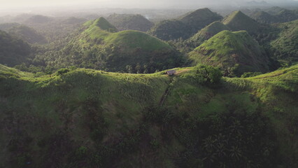 Green hill ranges aerial: mount top building with path at tropical greenery. Philippines landscape of small house at hiking way. Nobody Asian nature scenery at soft light drone shot