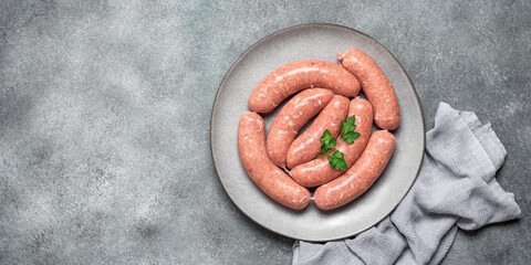 Raw homemade sausages in a plate on a gray grunge background. Top view, flat lay, copy space. Banner