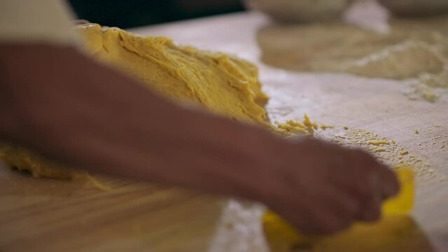 Hands of a Latin man, with a bakery instrument, collect the dough residue stuck on the table and integrate it into the main dough portion.