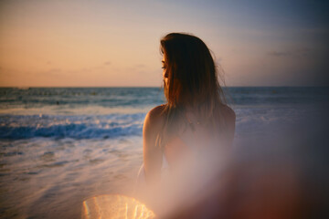A contemplative woman looks out to the sea as the golden hour sun bathes her in a warm, ethereal...