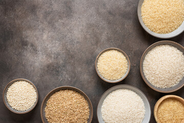 Set of different varieties of raw rice in bowls on a dark rustic background. Top view, copy space.