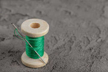 wooden spool with green thread and sharp needle