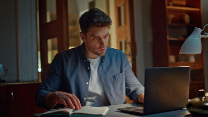 Focused man working laptop at night apartment closeup. Serious guy writing notes