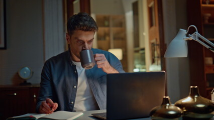 Pensive startuper drinking tea in night home office closeup. Guy holding pen
