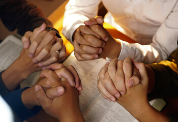 Christian family sitting around a wooden table with open bible page and holding each other's hand...