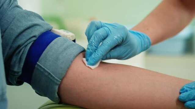Female nurse in medical gloves wiping with cotton wool vein, wipes place where will take blood for analysis. Closeup of doctor prepares patient hand to draw blood from vein. Shooting in slow motion.