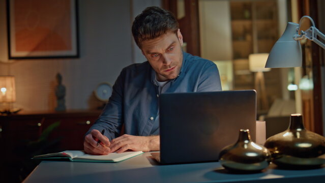 Online student studying night home looking laptop closeup. Man making notes