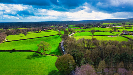Fototapeta na wymiar Aerial view of lush green countryside with patchwork fields under a partly cloudy sky.