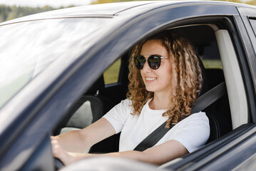 young beautiful smiling woman driving car, attractive caucasian woman in white t-shirt and black sunglasses