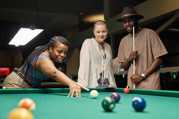 Portrait of smiling African American woman enjoying playing pool with diverse group of three friends copy space