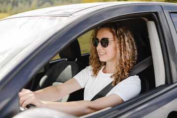 Fototapeta na wymiar young beautiful smiling woman driving car, attractive caucasian woman in white t-shirt and black sunglasses