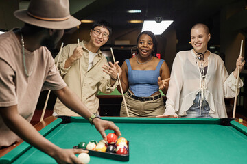 Diverse group of cheerful young people playing pool together standing round table