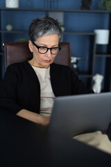 A pensioner, embracing education, works on her laptop at home, exemplifying lifelong learning. - 782448255