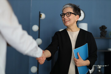professional portrait, a smiling businesswoman confidently shakes hands, surrounded by paperwork and exuding success.