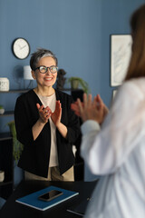 Obraz premium A smiling businesswoman claps joyfully, radiating confidence and success in her professional portrait.