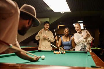 Multiethnic group of emotional people watching friend playing pool and taking shot copy space - 782448448