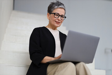 A mature businesswoman embraces technology, working online from her office, embodying professionalism and modern lifestyle.